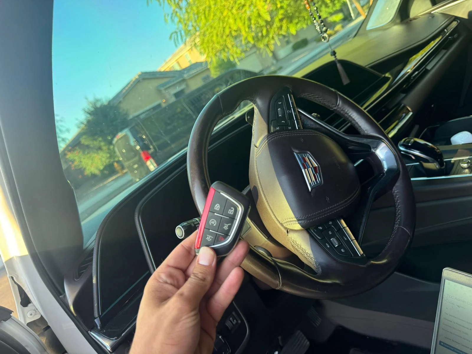 A hand holding a car key fob beside a Cadillac steering wheel, from the business's gallery